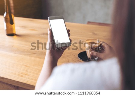 Mockup image of a woman's hand holding white mobile phone with blank desktop screen and coffee cup in cafe