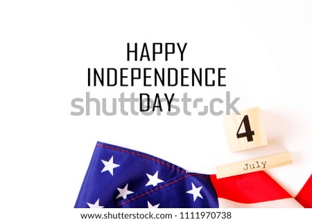 Ruffled American flag and wooden cube calendar with 4th of July congratulations. Happy Independence Day greeting card text on white copy space background. Patriotic composition, top view, close up.