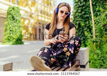 Urban young woman enjoying in the music on the park while sitting on the bench
