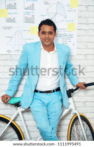 Elegant Indian businessman posing with bicycle against white brick wall with strategic plan on it