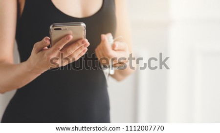 Closeup of slim woman in sportswear holding smartphone and earphones