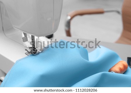 Sewing machine with fabric on table in tailor workshop, closeup