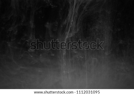 White liquid in water on a black background.