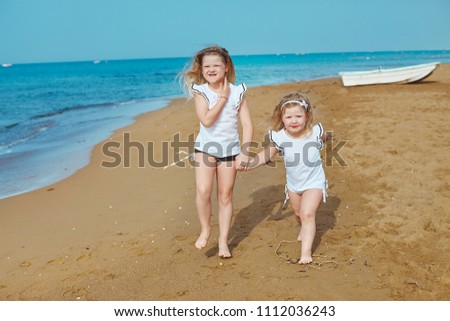Two cute blonde caucasian sisters are playing on sandy beach