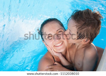 cute little caucasian kid kissing his happy smiling mother in summer azure pool in resort