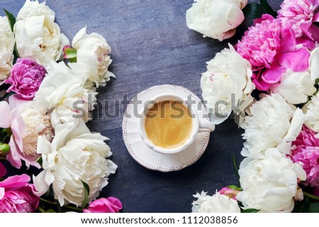 A cup of coffee and peony flowers on dark wooden background. Top view, copy space. Toned image