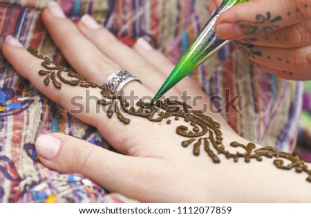 Artist painting traditional indian henna tattoo on woman hand, closeup picture, focus on mehndi artwork