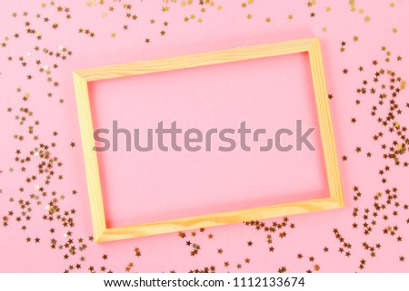 A wooden empty frame on a pastel background surrounded by shiny decorative stars and balls.