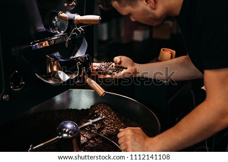 Man working at coffee production. Barista controling coffee grounds roasting process. Royalty-Free Stock Photo #1112141108