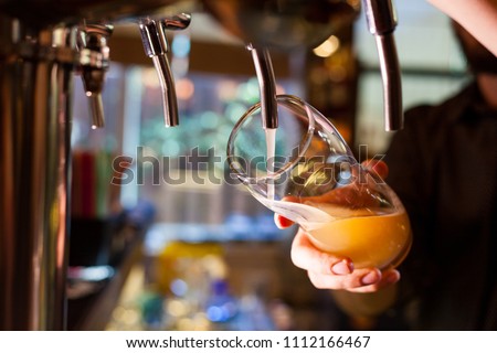 The barman pours light unfiltered beer from the tap Royalty-Free Stock Photo #1112166467