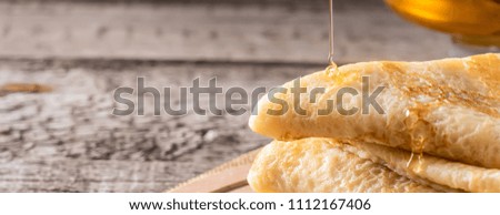 Spoon of honey flowing on stack of Thin lace Pancakes  Food concept holiday Shrovetide Maslenitsa homemade pastries on wooden board close-up