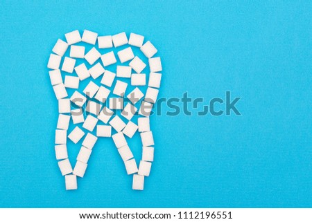 Sugar destroys tooth enamel and leads to tooth decay. Sugar cubes are lined in the form of a tooth on a blue background.