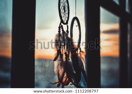 Two dream catchers hanging on the window at sunset time. Boho chic, hope freedom and dream concept.