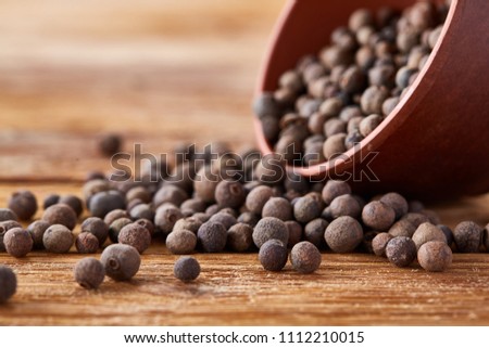 Overturned clay bowl with dried allspice berries on rustic wooden background, close-up, macro, shallow depth of field.