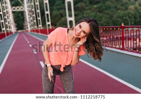 Stylish girl listening music during workout. Outdoor photo of magnificent young lady holding phone after training.