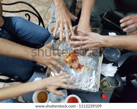 Top view of people sitting around the table and stretching hands to last piece of pizza