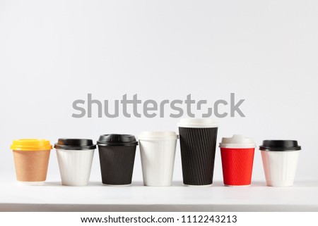 Disposable coffe cups different colors and sizes in a row on white background with copy space