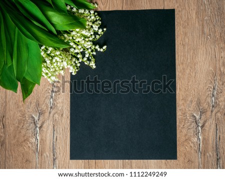 Bouquet of lilies of the valley on a wooden background and an empty piece of black paper