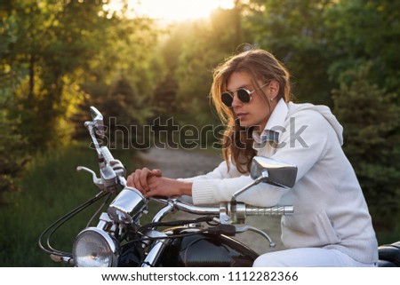 Biker wearing sunglasses and jacket at wheel of a motorcycle. Guy with long hair and an earring. Stop on road trip.