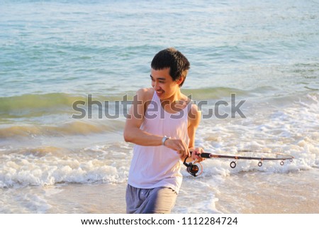 Young man  fishing in ocean surf at sunset.