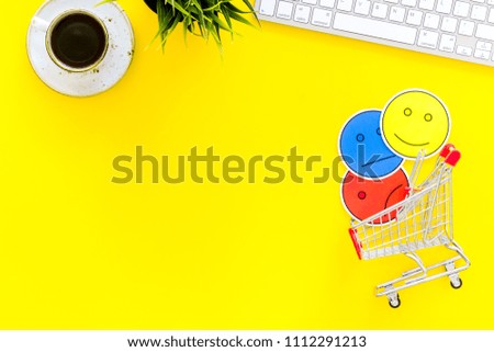 Client feedback concept. Emoji smiling, neutral, sad face near shopping cart on work desk on yellow background top view copy space