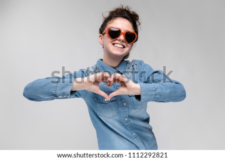 Young brunette girl with glasses in the form of a heart. The hairs are gathered in a bun. The girl folded her heart.
