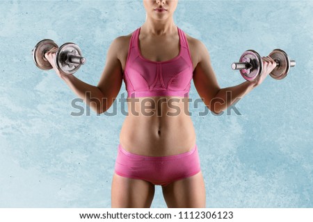 Beautiful young woman doing exercises with dumbbells.