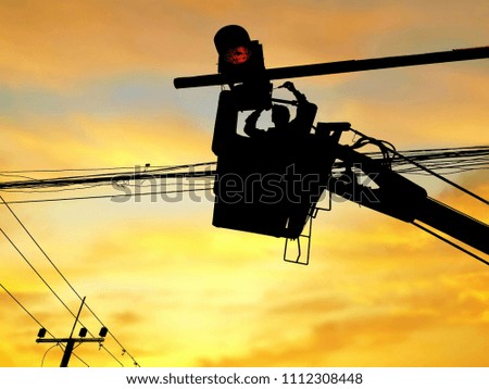 Silhouette of electrician in basket of cable car is repairing hanging traffic light box with blurred sunrise sky background on technology and development concept 