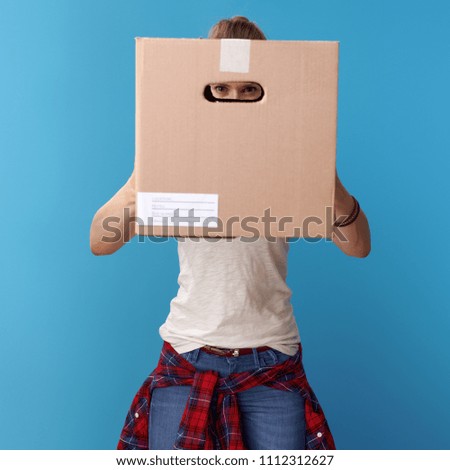 active hipster in white shirt looking through a cardboard box isolated on blue