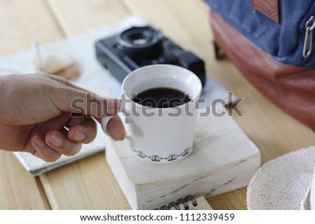 Plan your trip with morning coffee -Stock image Human hand, coffee mug, backpack, map, vintage camera, cap, us passport