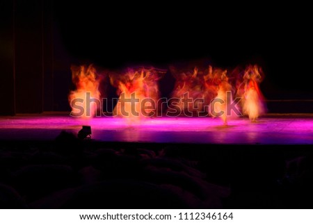A group of people dancing on stage against black background. Photograph is taken with long expose. 