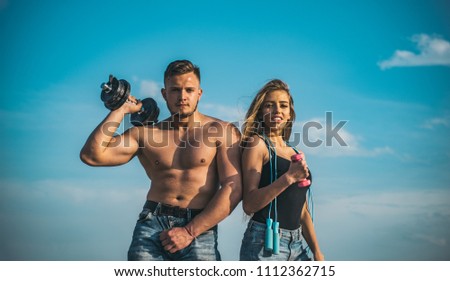 Couple training outdoors, sport and health concept. Man with muscular torso and blond smiling girl lifting dumbbells. Family of bodybuilders working out in open air over blue sky.