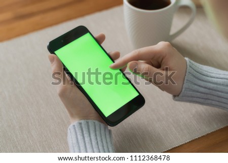 close-up hand holding phone white screen over work table