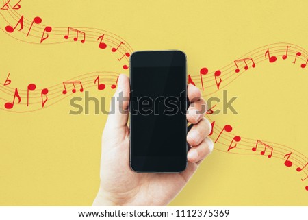 Male hand holding empty cellphone on yellow background with notes. Music, leisure, device and entertainment concept. Mock up 