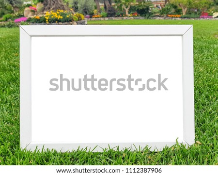 Empty white billboards or white frame with copy space on green grass in spring natural garden with colorful blurred flowers background.