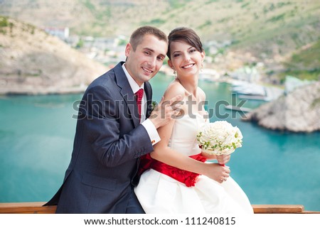 Young couple in love the bride and groom with a bouquet posing on the background beautiful mountains and bays of the wedding day in the summer. Enjoying a moment of happiness and love.