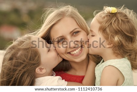 Summer vacation, leisure, activity, lifestyle. Daughters kiss mother on natural landscape. Happy childhood, family, love. Mothers day concept. Woman and girls sit on bench.
