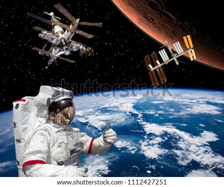 Astronaut shows the thumbs-up about flying to Mars. Space station on the backdrop.  Space craft in outer space.. The elements of this image furnished by NASA.
