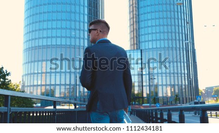 A young handsome businessman holds a bottle of water in his hand, in a suit, a skyscraper background