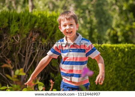 Cute and adorable Caucasian boy in a striped shirt playing in the park in the summer.