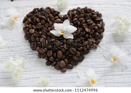 Heart of coffee beans laid out on a white wooden background with white hydrangea flowers and orchids