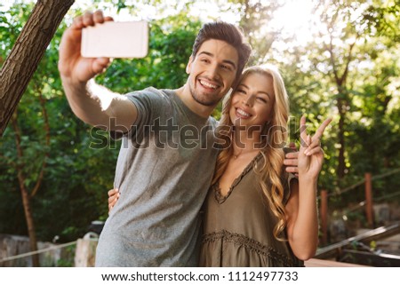 Picture of Cheerful lovely young couple posing together and making selfie on smartphone outdoors