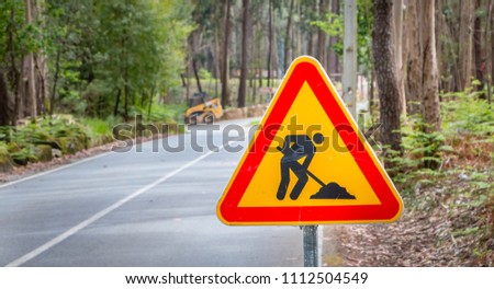 worn temporary road sign showing work on a small road in the forest