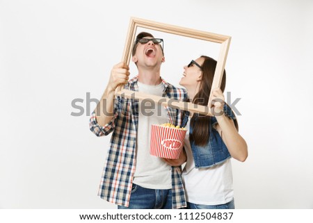 Young laughing couple, woman and man in 3d glasses and casual clothes watching movie film on date, holding bucket of popcorn and picture frame isolated on white background. Emotions in cinema concept