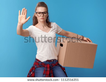 young woman in white shirt with a cardboard box showing stop gesture isolated on blue background