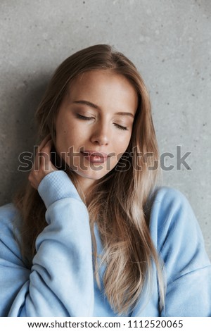 Picture of young beautiful woman standing over grey wall background with eyes closed.