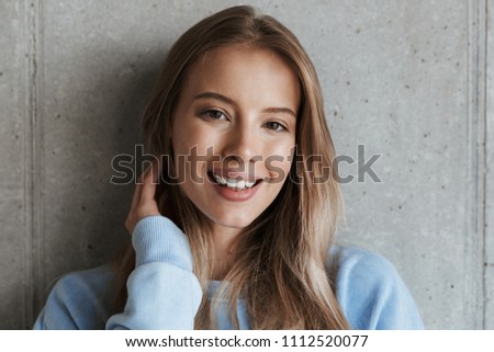 Picture of young cheerful happy pretty woman standing over grey wall background looking camera.
