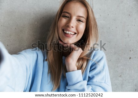 Picture of young cheerful happy pretty woman standing over grey wall background make selfie by camera.