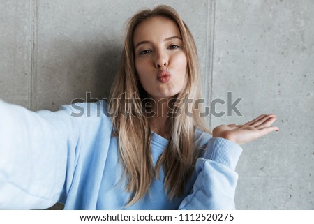 Picture of young happy pretty woman standing over grey wall background make selfie by camera blowing kisses.