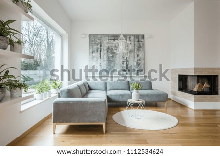 Spacious white living room interior with grey corner couch, big modern art painting and fireplace